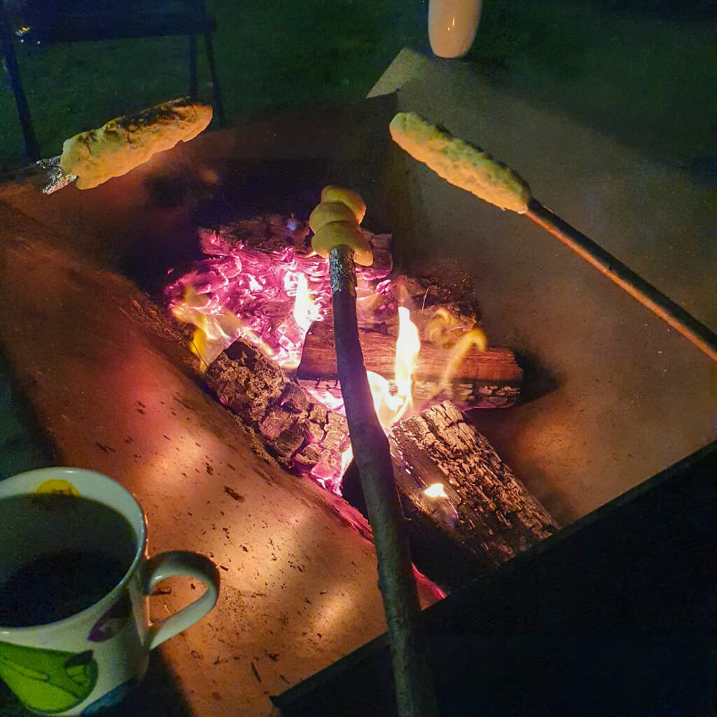 120 kg schwerer Feuertisch von Rostige Aussichten in Walzblau mit brennenden Holzscheiden und Stockbrot